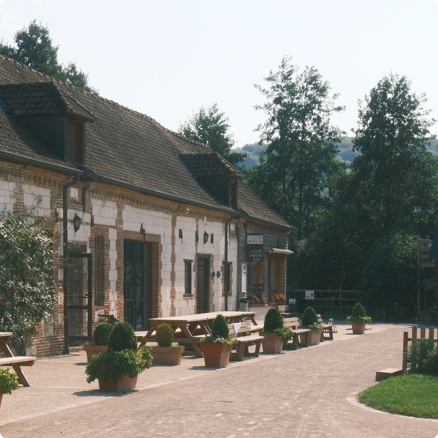 Bâtiments de ferme en pierre et brique, tables de pique-nique et panneau Club House