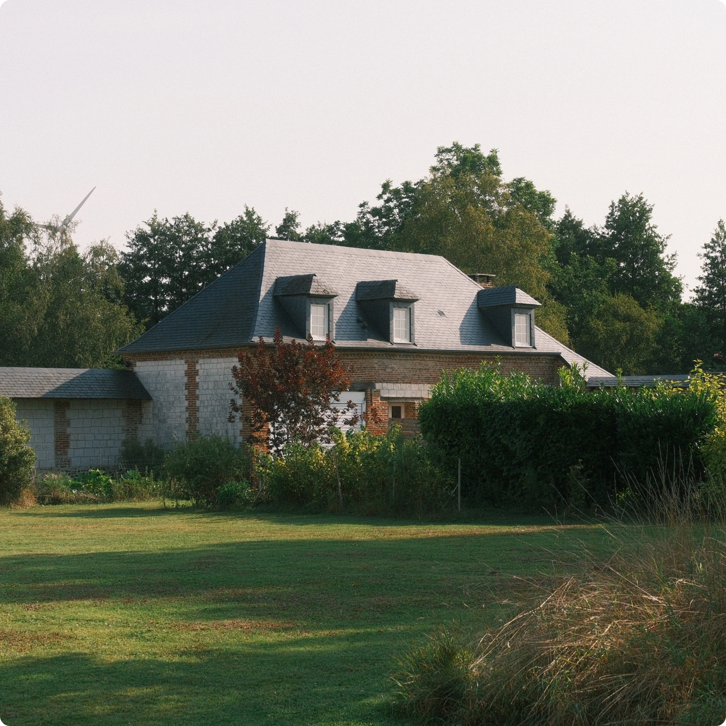 Maison de campagne en brique et pierre au toit d'ardoise, pelouse et haies