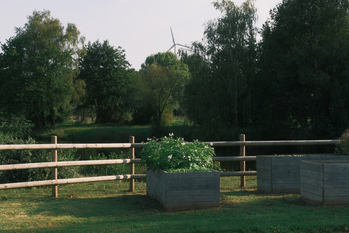 Wooden fence, flower planter, tall green trees and a wind pump