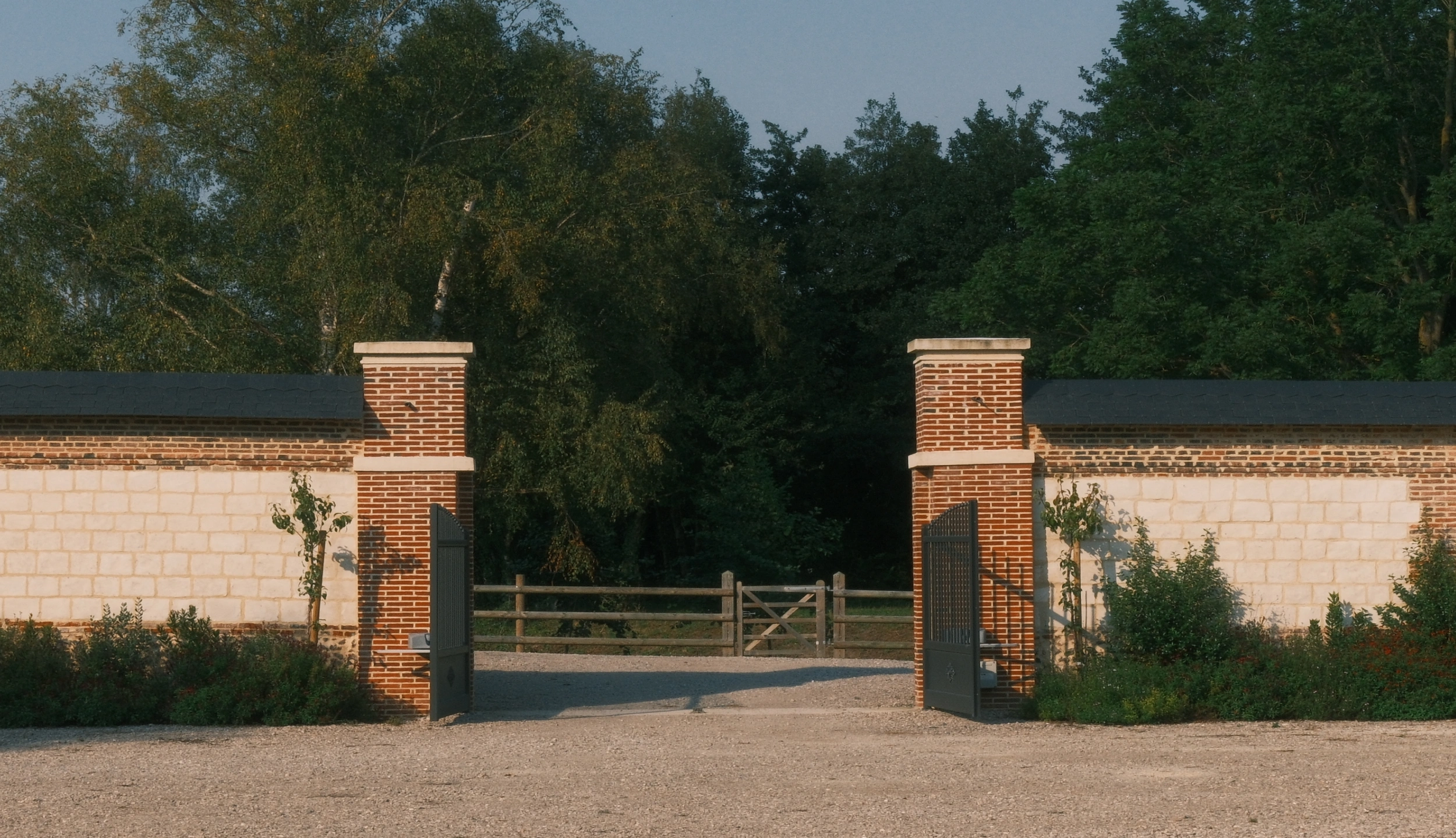 Two brick gate pillars with open gates between white walls