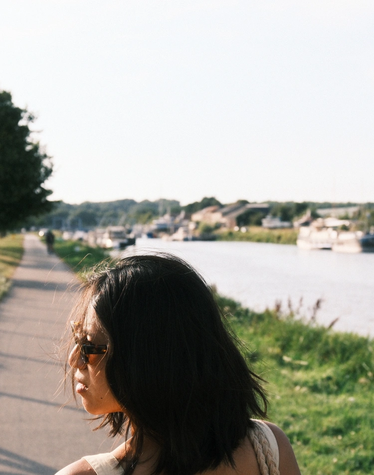 Woman in profile on a path along a river lined with boats