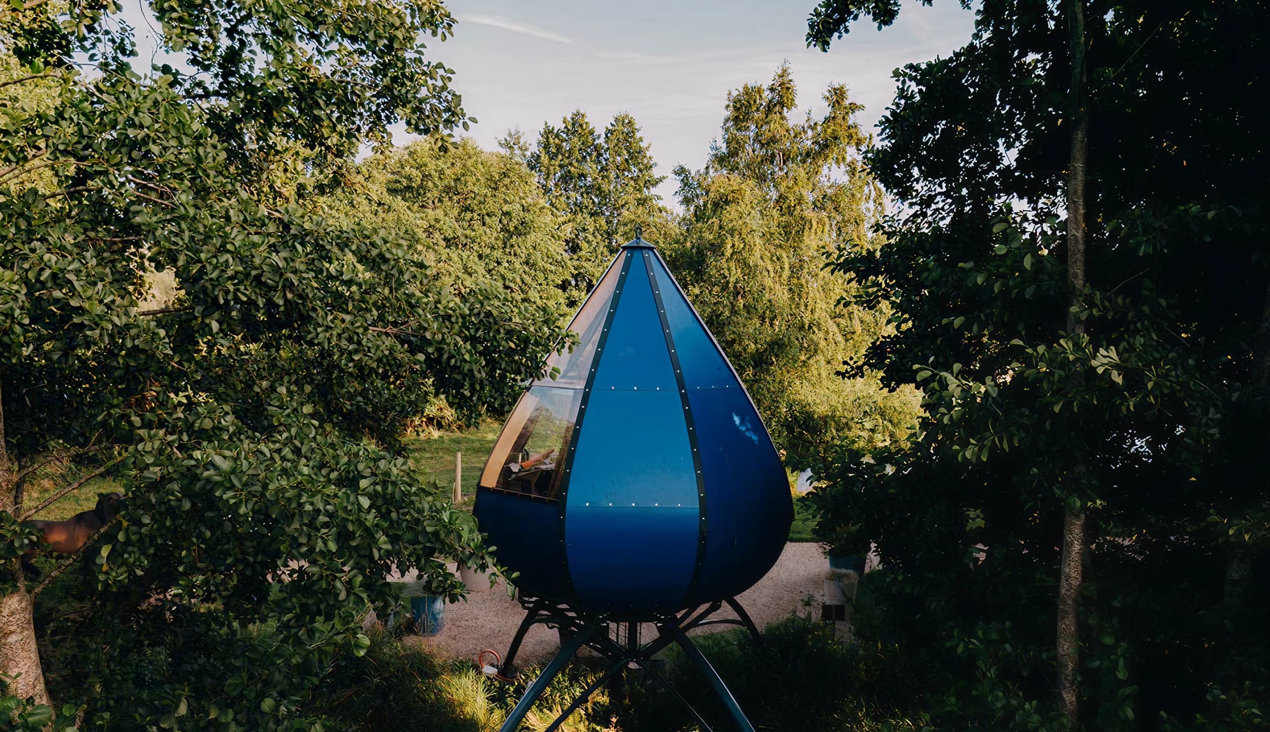 Cabane bleue en forme de goutte suspendue sur pieds au-dessus d'un étang