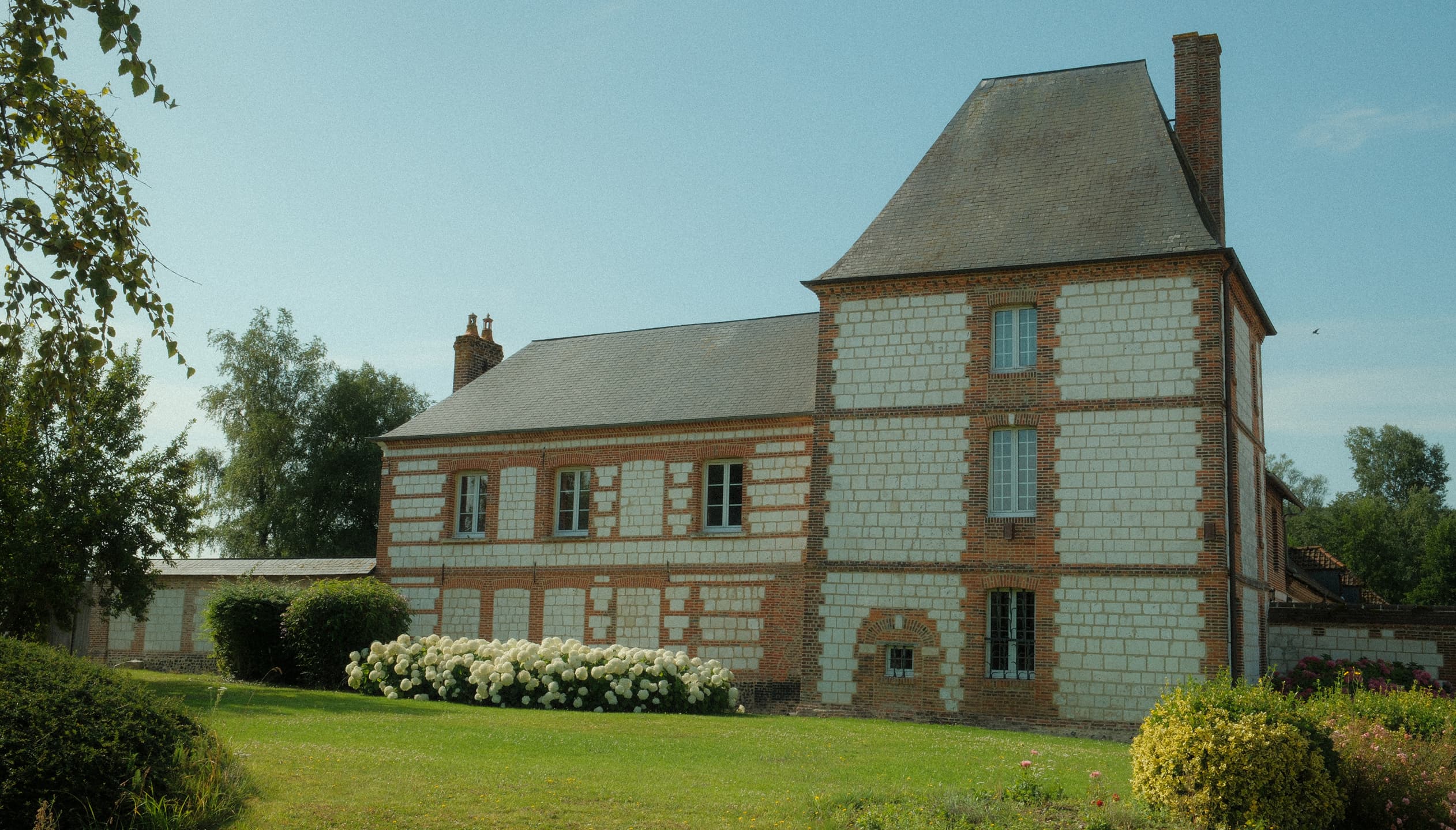 Brick and stone manor with a tower, white hydrangeas and lawn