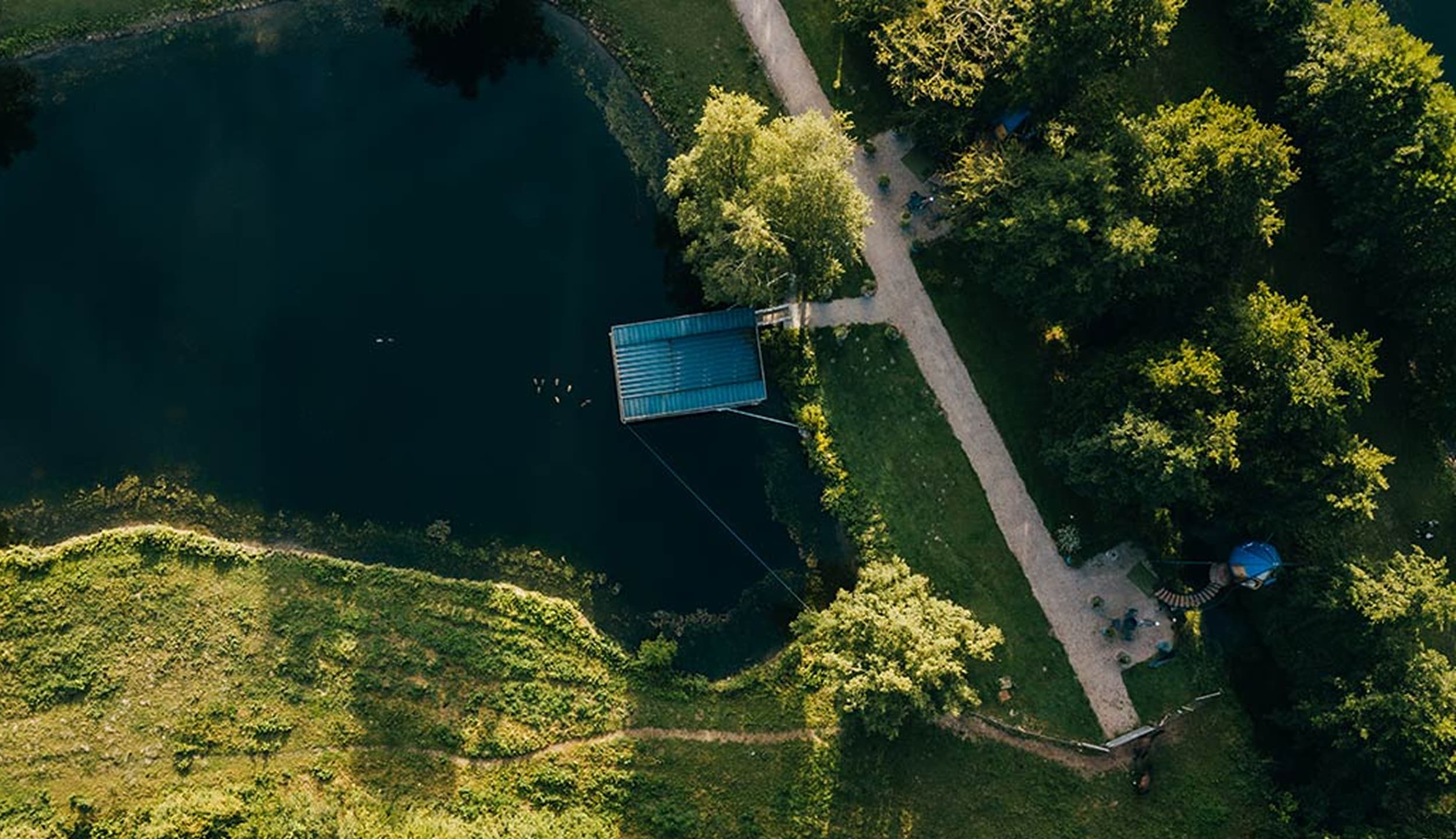 Vue aérienne d'une cabane sur l'eau reliée à des chemins serpentant entre les arbres