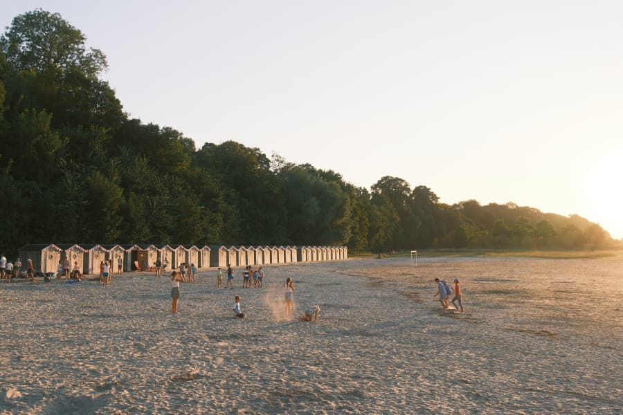 Beach of Saint-Valery-sur-Somme, children running on the sand, with a sunset and the beach huts in view.
